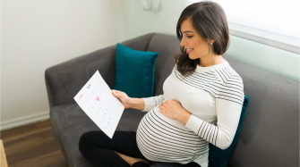 Une femme enceinte assise sur son canapé, regardant le calendrier de grossesse